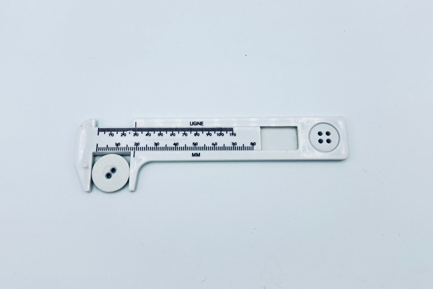 White plastic button gauge with white linen button in calipers