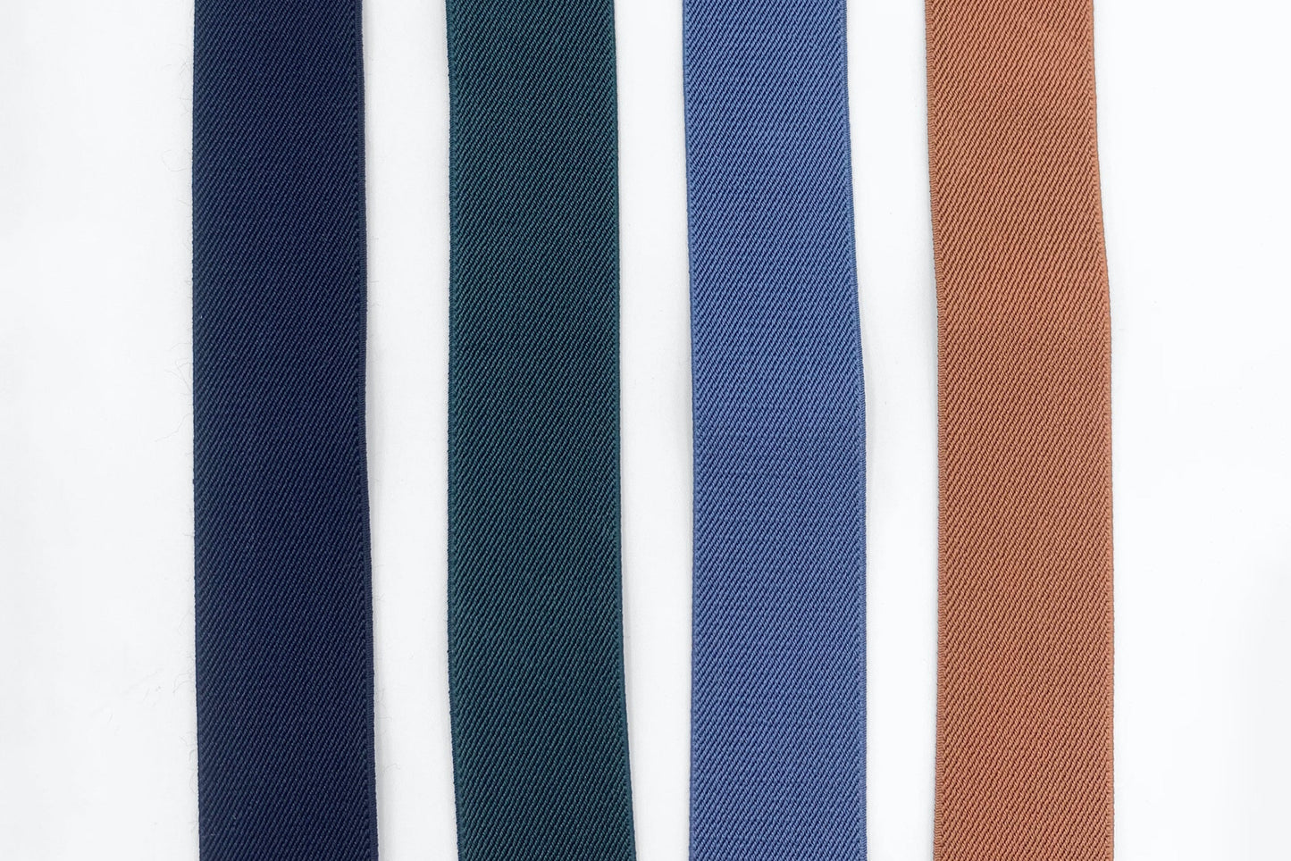 4 colors of elastic suspenders laid out next to each other; Black, Forest Green, Slate Blue and Camel