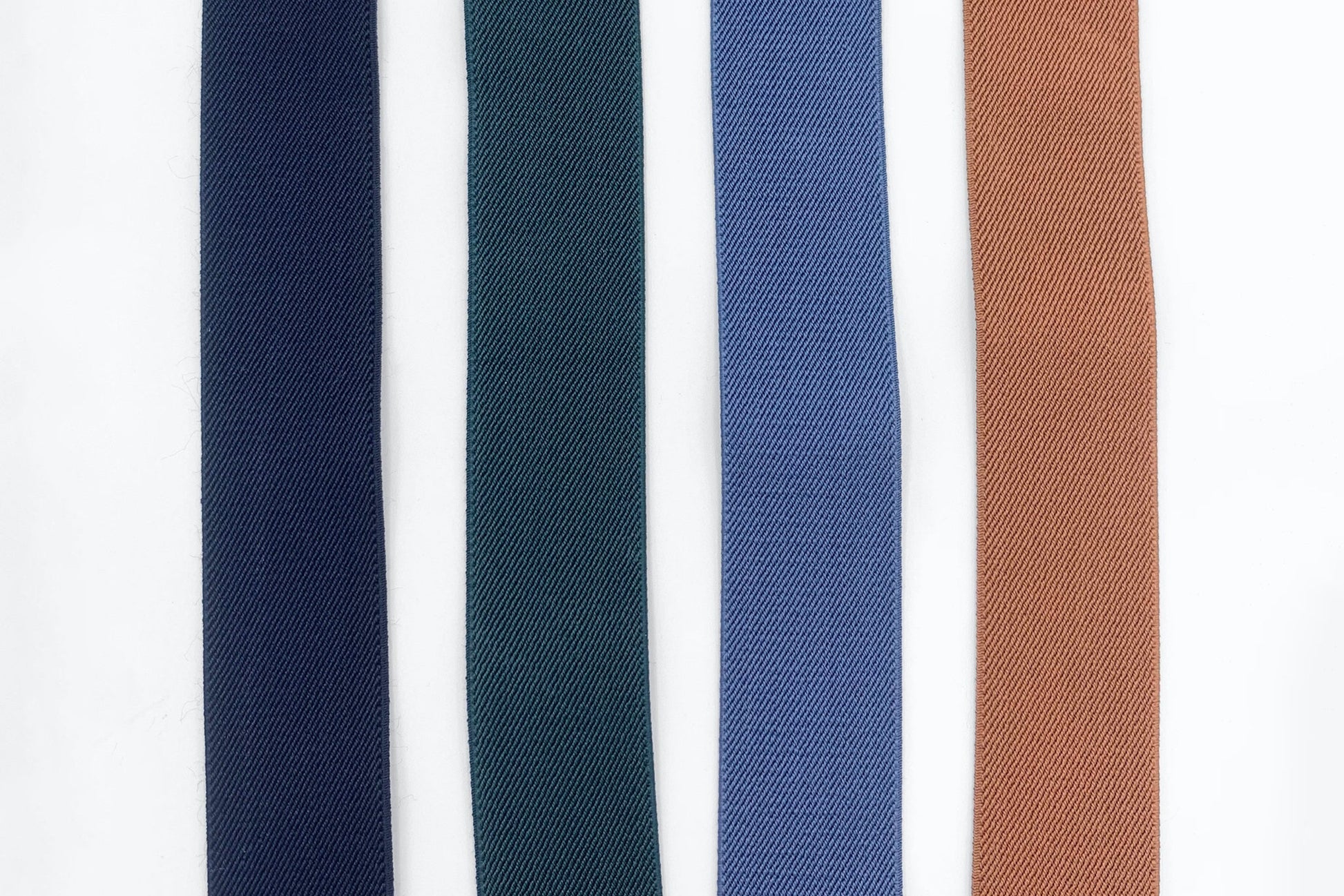 4 colors of elastic suspenders laid out next to each other; Black, Forest Green, Slate Blue and Camel